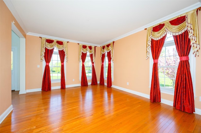 empty room featuring crown molding, baseboards, a healthy amount of sunlight, and light wood-type flooring
