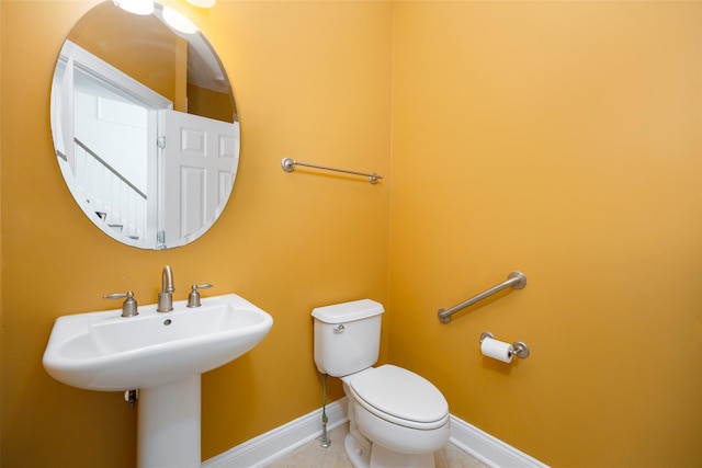 half bath featuring toilet, baseboards, a sink, and tile patterned flooring