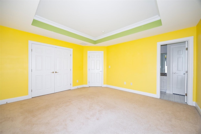 unfurnished bedroom featuring light colored carpet, ornamental molding, multiple closets, and a tray ceiling