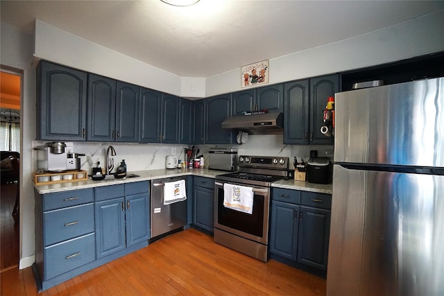 kitchen with light wood-type flooring, light countertops, under cabinet range hood, appliances with stainless steel finishes, and blue cabinetry