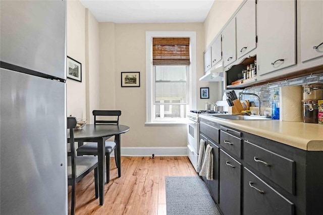 kitchen featuring backsplash, light wood-type flooring, a sink, baseboards, and light countertops