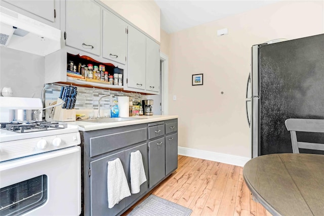 kitchen with a sink, light wood-style flooring, freestanding refrigerator, white gas stove, and under cabinet range hood
