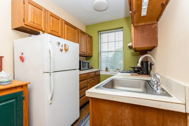 kitchen featuring freestanding refrigerator, a sink, light countertops, and brown cabinetry
