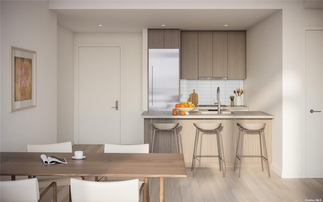 kitchen with modern cabinets, tasteful backsplash, light wood-type flooring, a sink, and a breakfast bar
