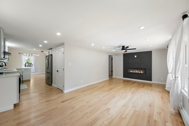 unfurnished living room with recessed lighting, a ceiling fan, light wood-type flooring, a large fireplace, and baseboards