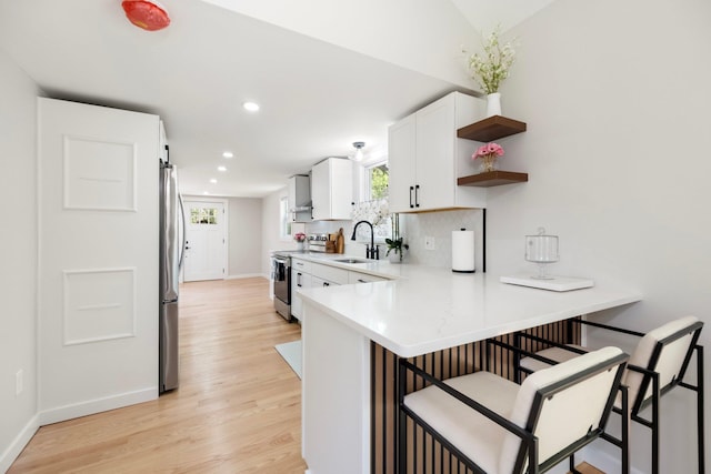 kitchen with stainless steel appliances, a kitchen bar, a sink, light wood-style floors, and recessed lighting
