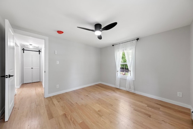 spare room with a ceiling fan, baseboards, a barn door, and light wood-style flooring
