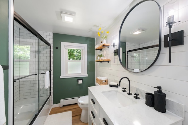 bathroom with a baseboard radiator, wood finished floors, vanity, toilet, and shower / bath combination with glass door