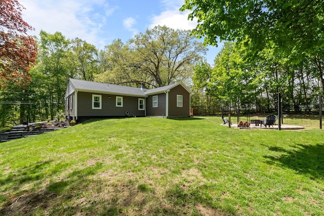 back of property with a fire pit, a lawn, and view of scattered trees