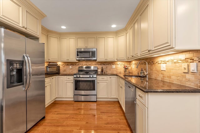 kitchen with appliances with stainless steel finishes, cream cabinetry, a sink, dark stone countertops, and recessed lighting