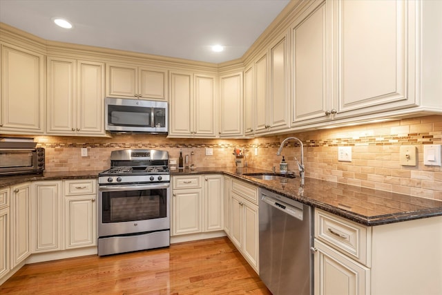 kitchen featuring appliances with stainless steel finishes, cream cabinetry, a sink, and dark stone countertops
