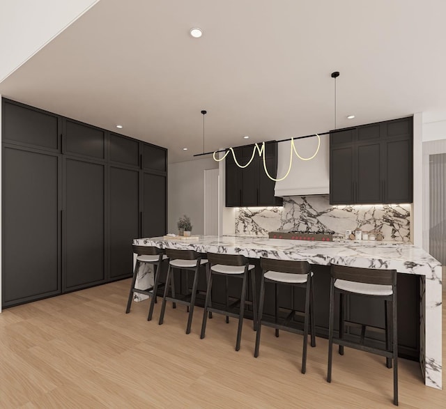 1629 Cedar Swamp Rd, Glen Head, NY 11545 - kitchen with range hood, decorative backsplash, a breakfast bar area, dark cabinets, and light wood finished floors