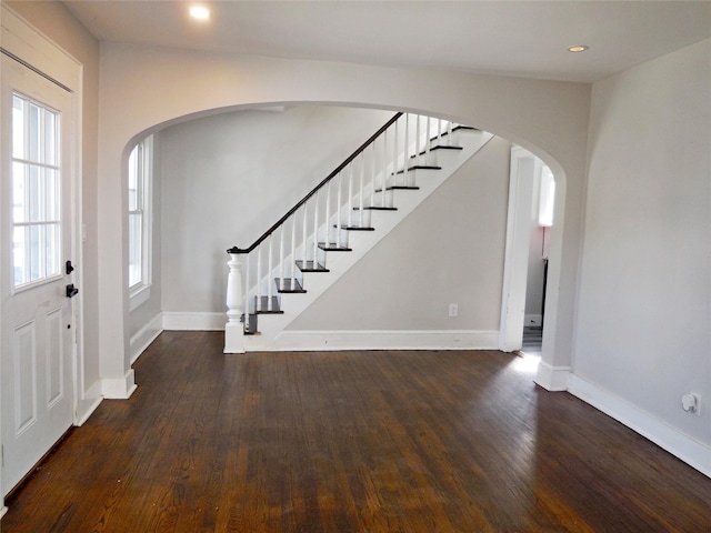 foyer entrance with stairs, arched walkways, baseboards, and dark wood finished floors