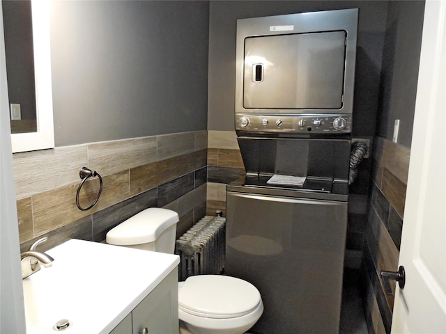half bath featuring vanity, stacked washer / dryer, toilet, tile walls, and radiator heating unit