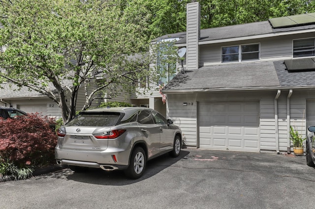 exterior space featuring a shingled roof, aphalt driveway, a garage, roof mounted solar panels, and a chimney