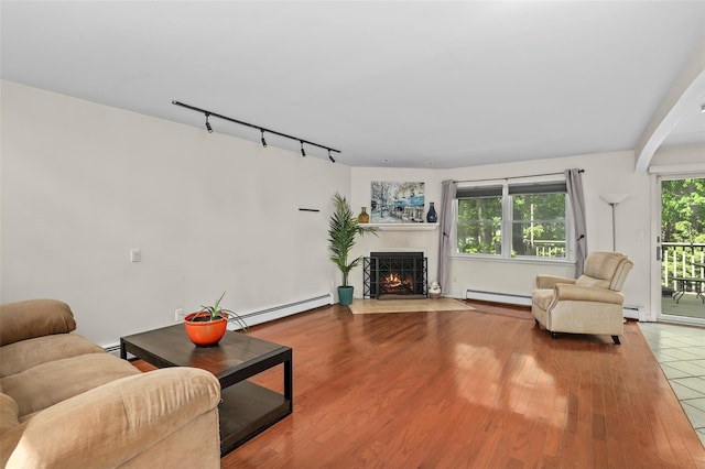 living area with a fireplace with flush hearth, a baseboard heating unit, track lighting, and wood finished floors