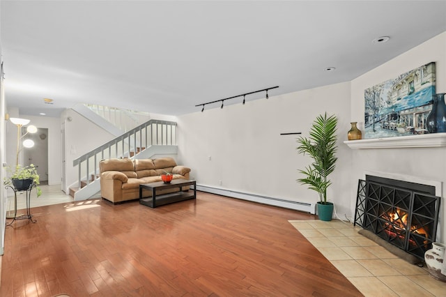 living area featuring wood-type flooring, rail lighting, a fireplace with flush hearth, a baseboard heating unit, and stairway