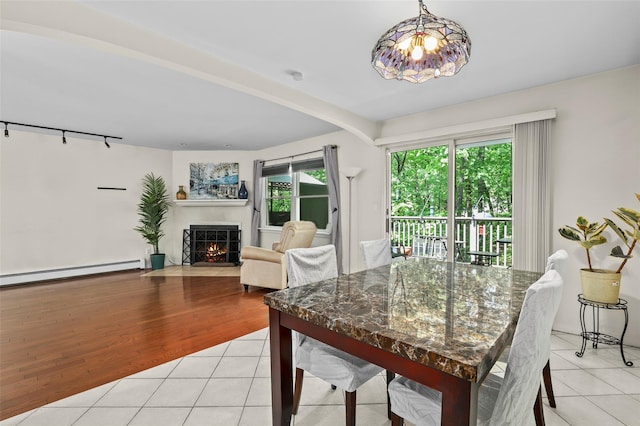 dining room with light tile patterned floors, a baseboard heating unit, rail lighting, and a fireplace with flush hearth
