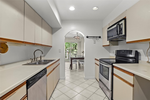 kitchen featuring appliances with stainless steel finishes, arched walkways, a sink, light tile patterned floors, and light countertops