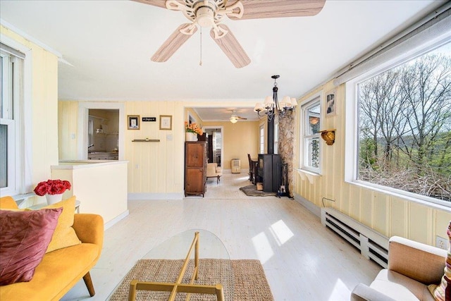 living room featuring ceiling fan, baseboard heating, a wood stove, light wood-type flooring, and baseboards