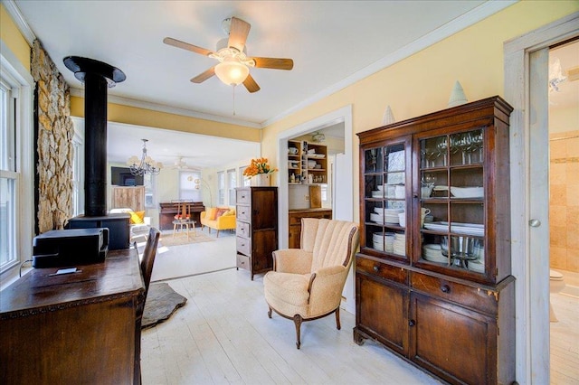 office featuring light wood-style floors, ornamental molding, a wood stove, and ceiling fan with notable chandelier