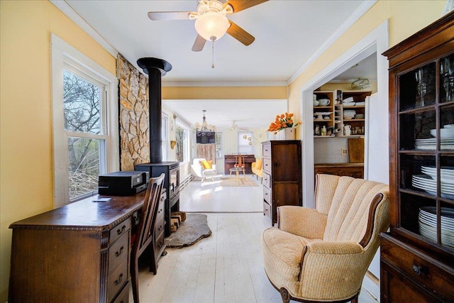 interior space with light wood-style floors, ornamental molding, a wood stove, and ceiling fan with notable chandelier