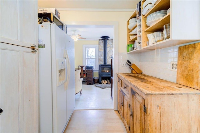 interior space with a wood stove, decorative backsplash, butcher block countertops, ceiling fan, and white fridge with ice dispenser