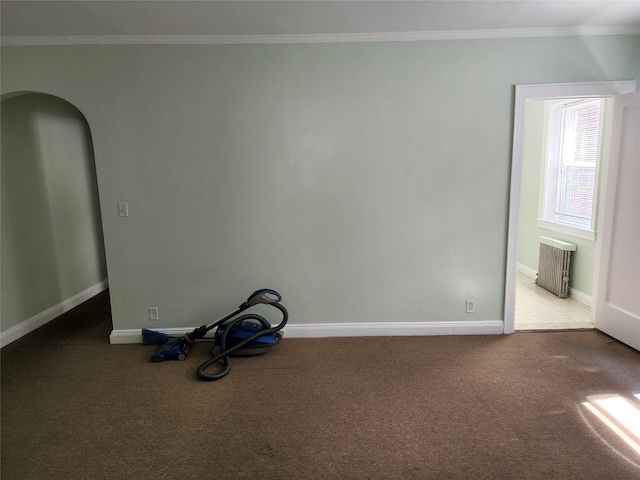 carpeted spare room featuring baseboards, ornamental molding, and arched walkways