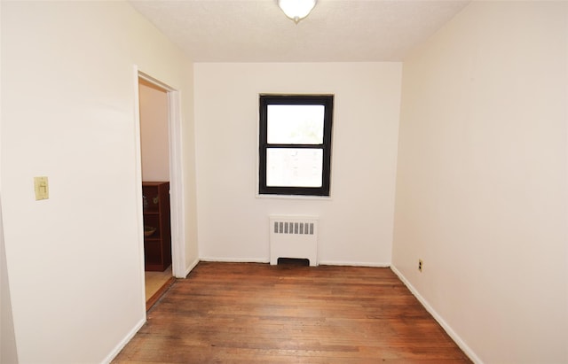 empty room featuring baseboards, radiator heating unit, and hardwood / wood-style flooring