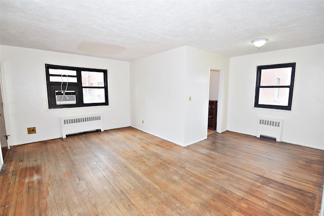 spare room featuring light wood-style floors, a textured ceiling, radiator, and baseboards