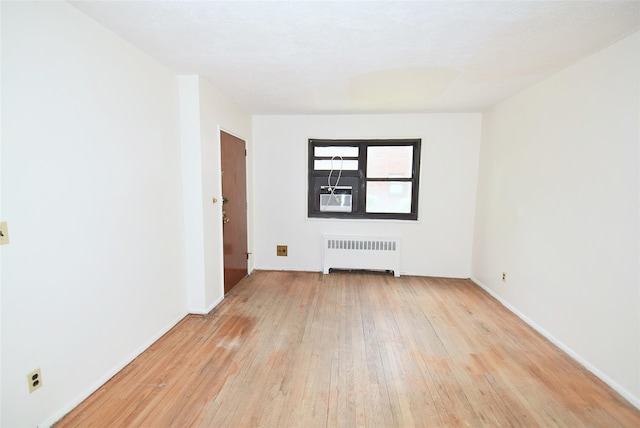 empty room with radiator heating unit, baseboards, and light wood-type flooring