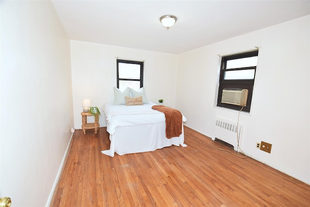 bedroom featuring light wood-style flooring, radiator heating unit, multiple windows, and cooling unit