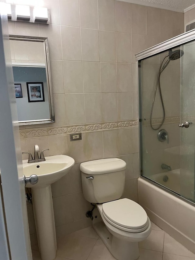 full bath featuring toilet, tile walls, tile patterned floors, and bath / shower combo with glass door
