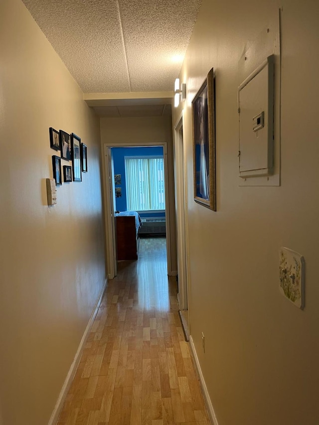 corridor with baseboards, light wood finished floors, and electric panel