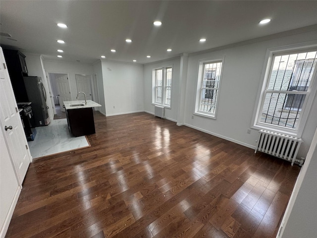 unfurnished living room with a sink, radiator, ornamental molding, and dark wood finished floors