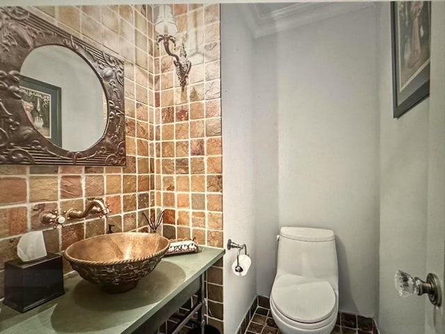 half bathroom featuring toilet, baseboards, ornamental molding, and a sink