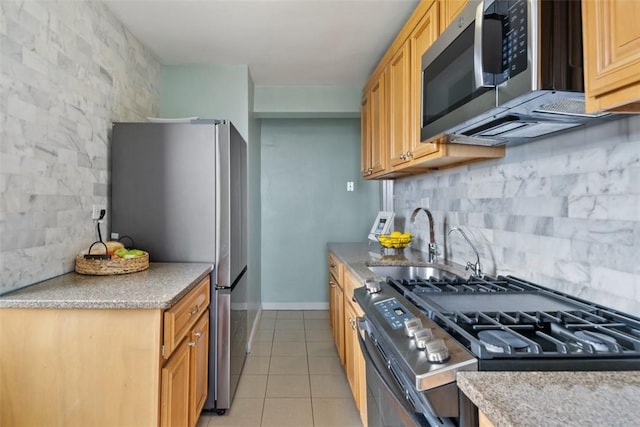 kitchen featuring baseboards, a sink, backsplash, light tile patterned floors, and stainless steel appliances
