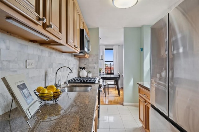 kitchen featuring appliances with stainless steel finishes, a sink, dark stone counters, baseboards, and light tile patterned floors