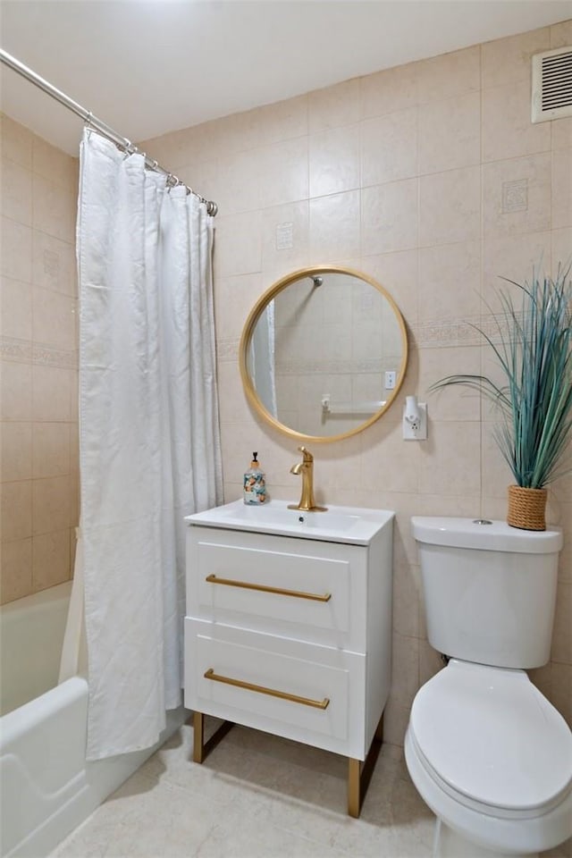 full bath with visible vents, vanity, toilet, tile walls, and shower / tub combo