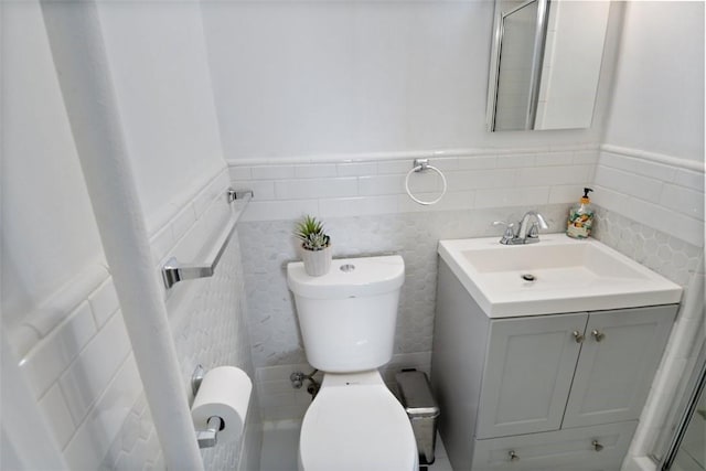 bathroom featuring vanity, wainscoting, toilet, and tile walls