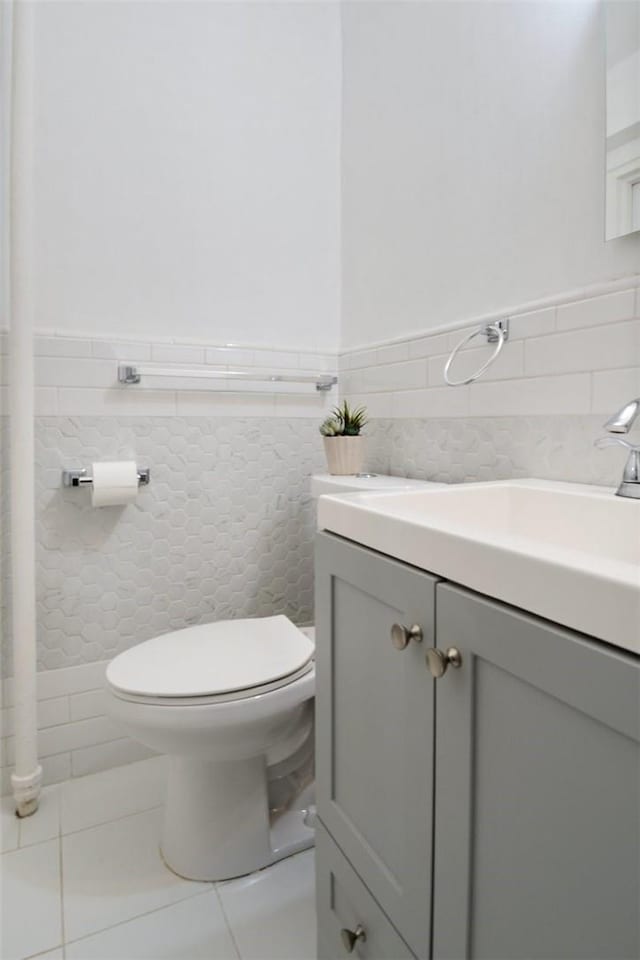 half bath featuring tile walls, tile patterned floors, vanity, and toilet