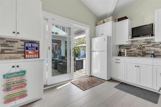 kitchen featuring freestanding refrigerator, lofted ceiling, a sink, white cabinets, and tasteful backsplash