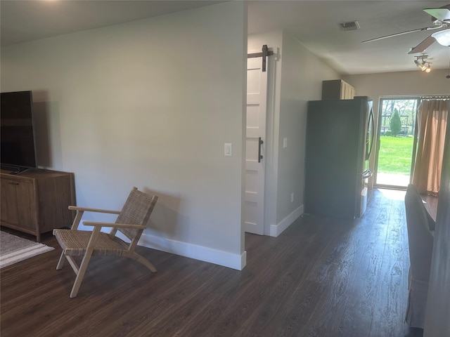 interior space with a barn door, visible vents, ceiling fan, dark wood-style floors, and baseboards