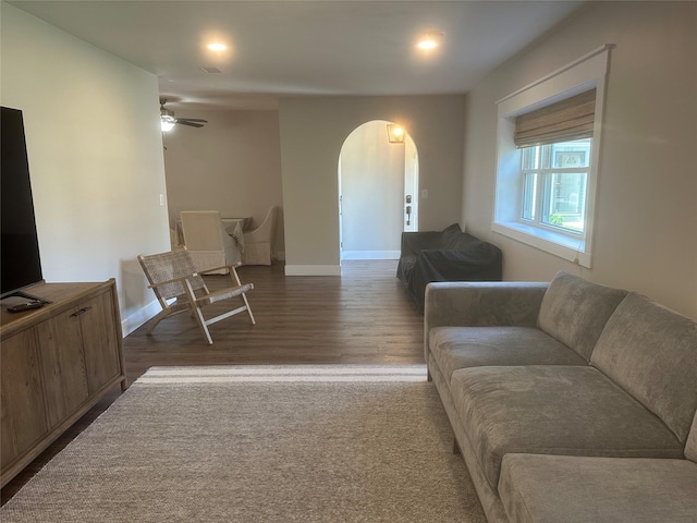 living area with arched walkways, dark wood-style flooring, baseboards, and ceiling fan