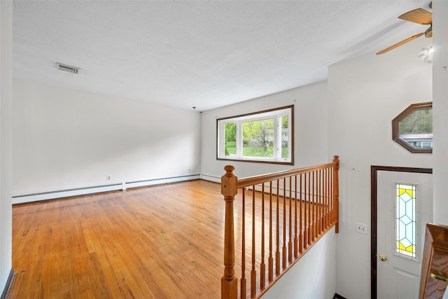 interior space with a baseboard heating unit, a ceiling fan, visible vents, and wood finished floors