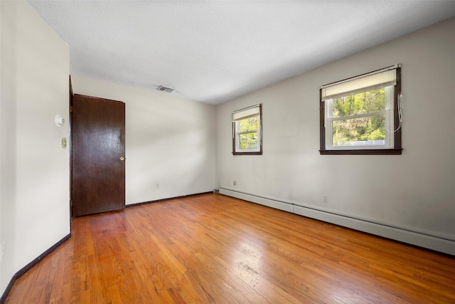 spare room with visible vents, a baseboard heating unit, baseboards, and wood-type flooring