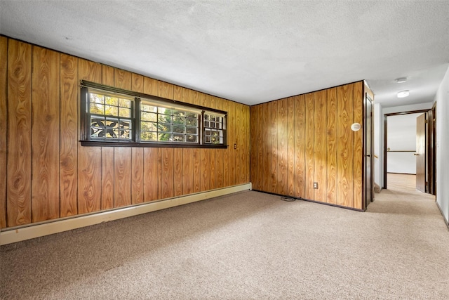 spare room with carpet, a textured ceiling, wooden walls, and baseboard heating