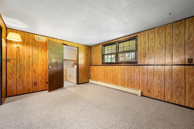 unfurnished room with carpet flooring, a textured ceiling, visible vents, a baseboard heating unit, and wooden walls