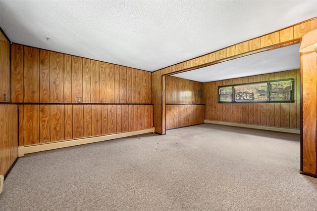 carpeted empty room with a baseboard radiator, a textured ceiling, baseboards, and wooden walls