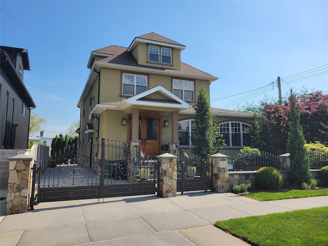 traditional style home featuring a shingled roof, a fenced front yard, a gate, and stucco siding